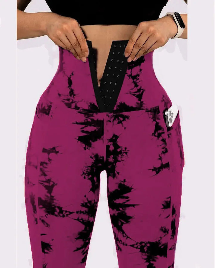Close-up of person wearing purple and black tie-dye waist trainer leggings with side pocket holding a smartphone