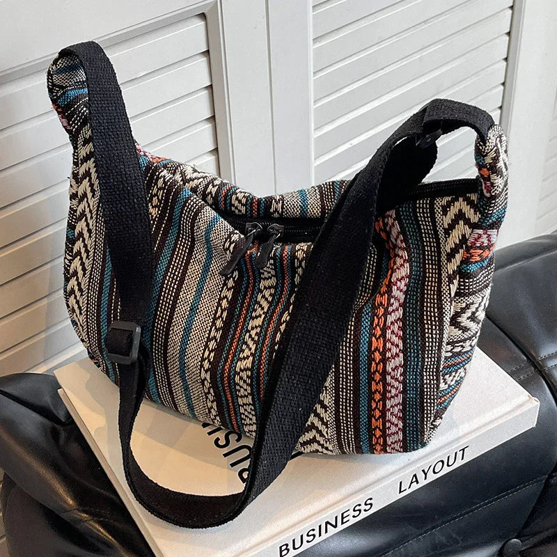 Ethnic patterned fabric shoulder bag with black strap placed on business layout book on black leather couch