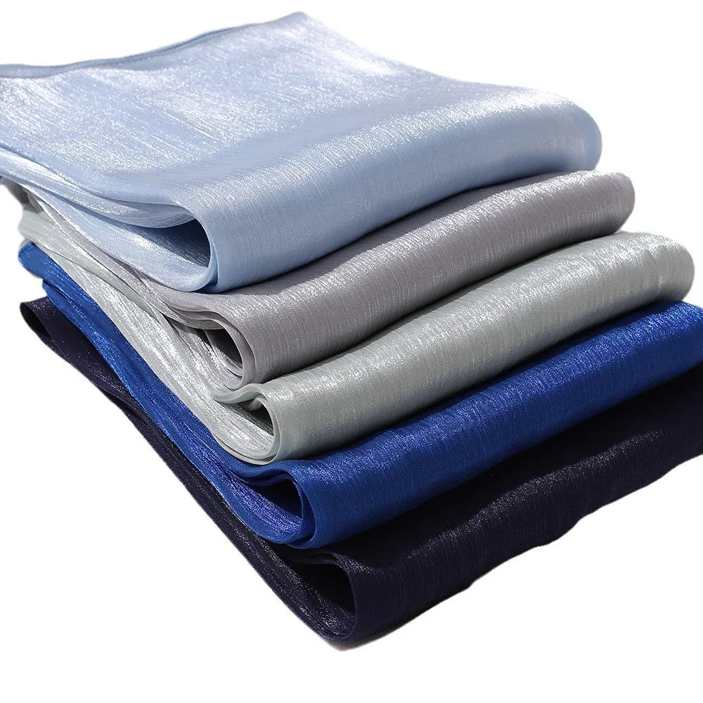 Stack of shiny folded fabrics in shades of blue and gray with smooth texture