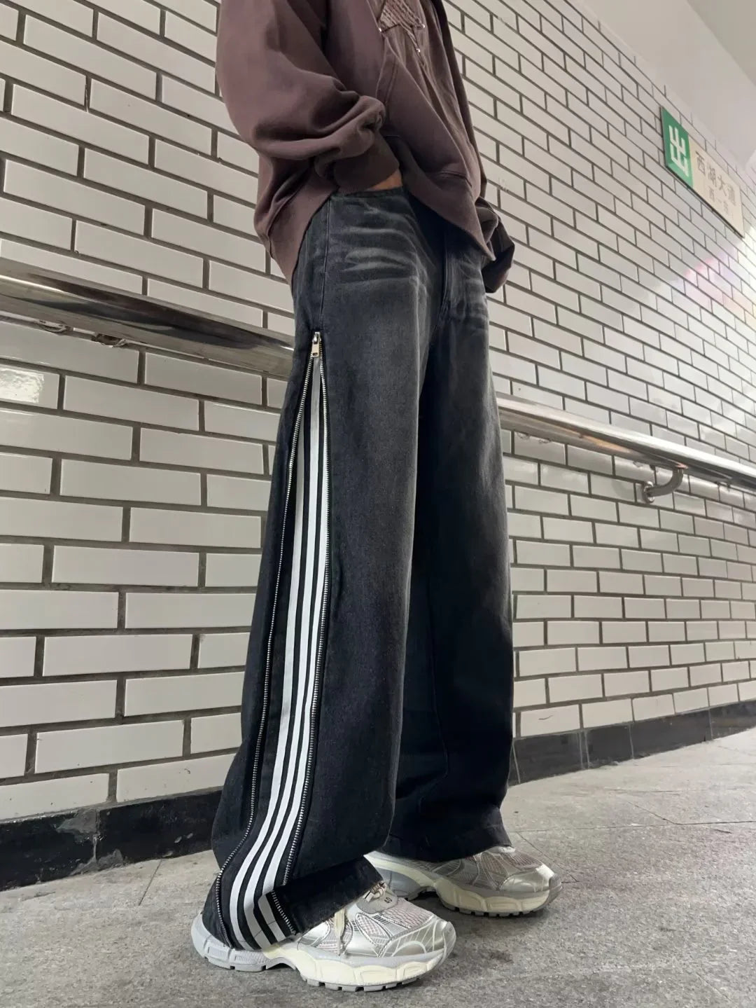 Person wearing black wide-leg pants with white stripes and zippers on sides, white sneakers, and brown sweatshirt