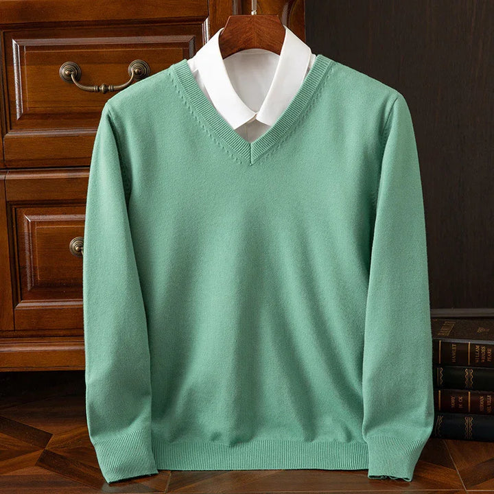 Mint green V-neck sweater over white collared shirt on wooden hanger with classic furniture background