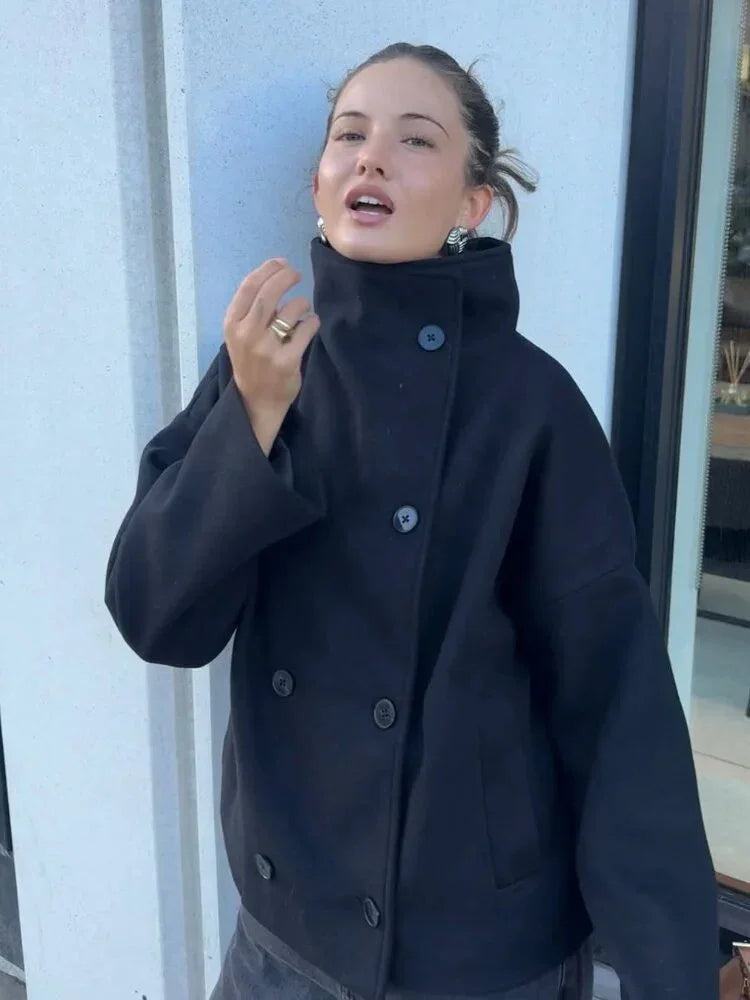 Young woman wearing a stylish black oversized coat with high collar and large buttons, posing outdoors