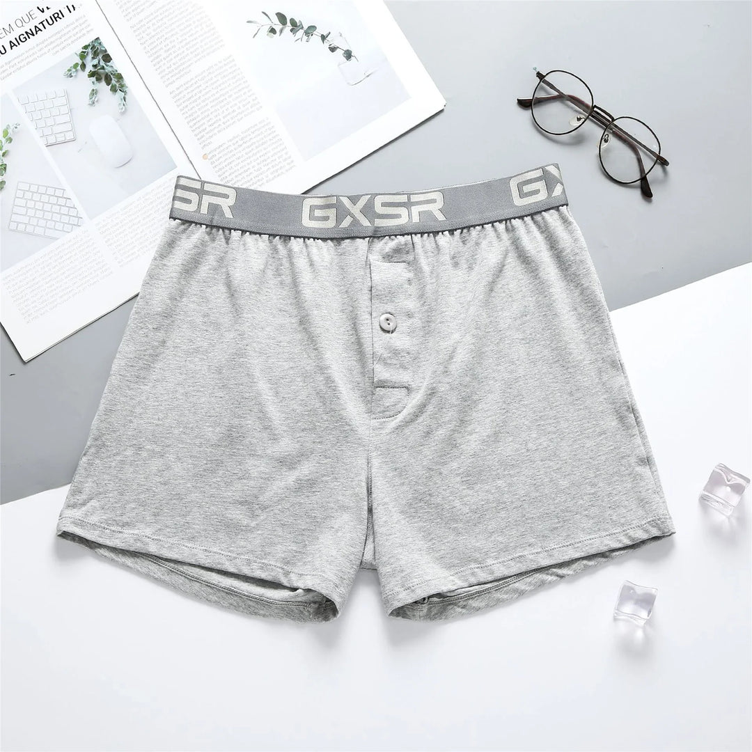 Light grey men's boxer shorts with GXSR waistband, button fly, on white and grey background with glasses and magazine