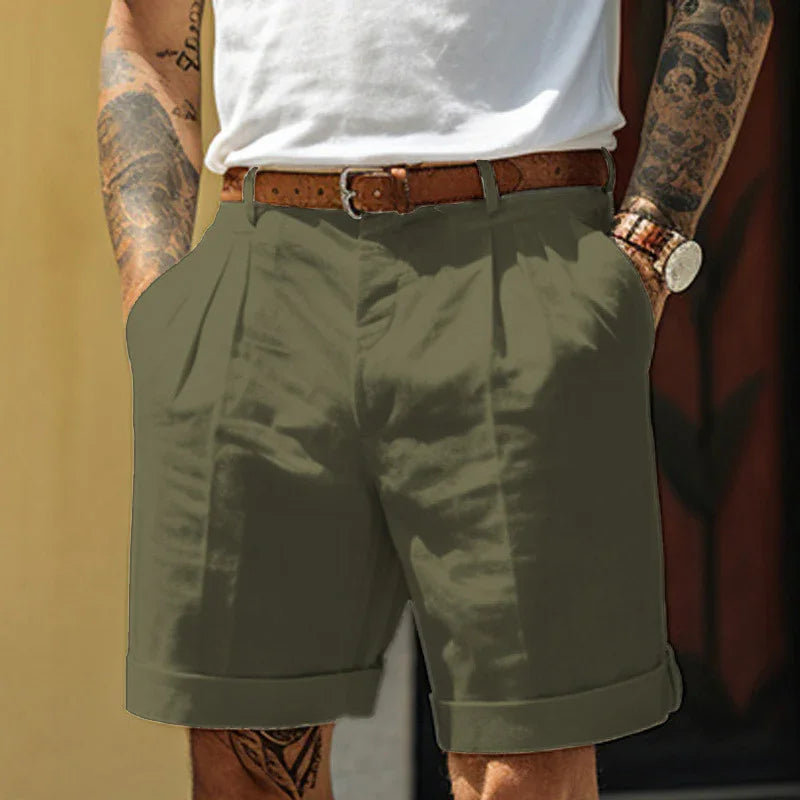 Man wearing olive green casual shorts with brown belt, white t-shirt, tattoos on arms, and wristwatch