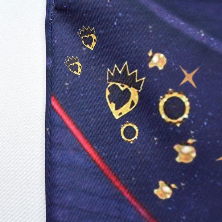 Close-up of navy blue fabric with gold heart crowned symbols and star-like patterns and red diagonal line