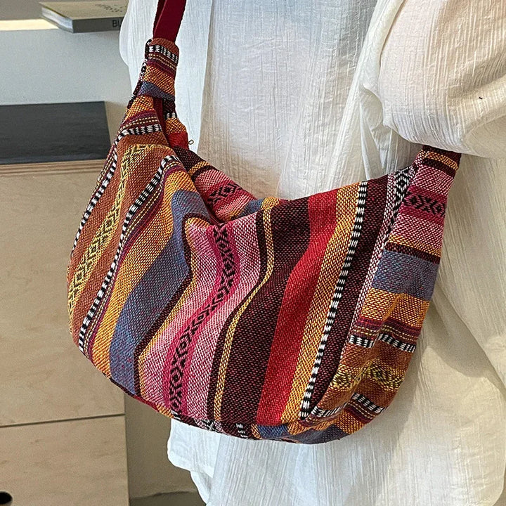 Colorful boho woven shoulder bag with geometric patterns worn over white textured fabric