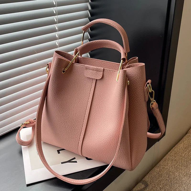 Stylish pink textured leather handbag with gold hardware, top handles, and detachable shoulder strap near window blinds