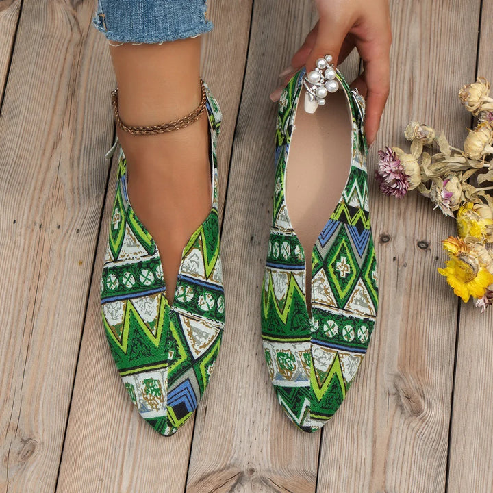 Pair of green patterned pointed flats with floral and geometric designs on wooden floor, one worn with anklet