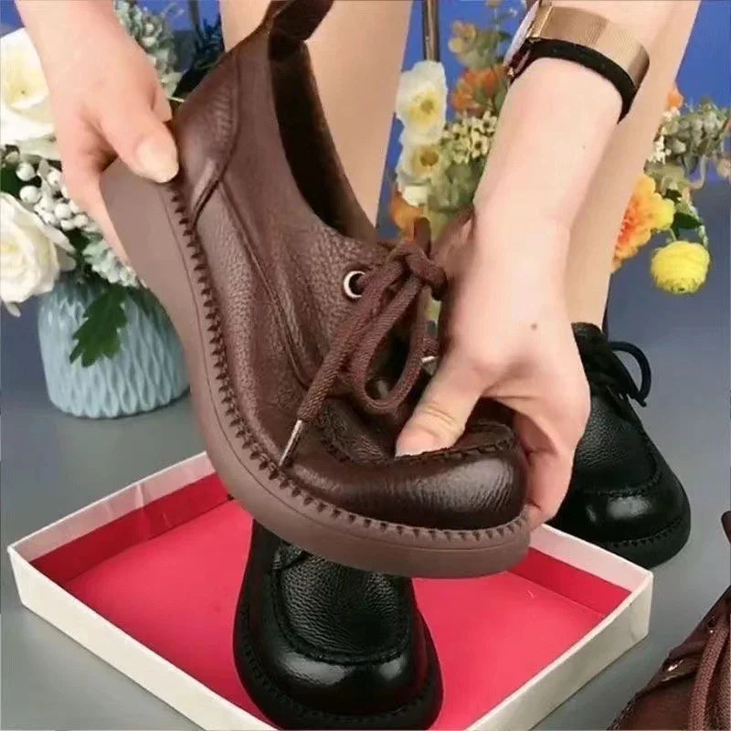 Hand holding flexible brown leather casual shoe with stitching, black shoe in background with flowers