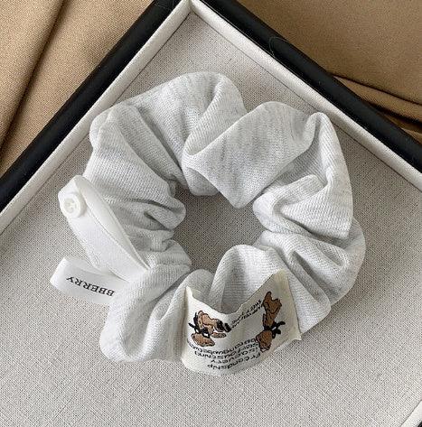 Light gray fabric scrunchie with Burberry tag and embroidered cartoon dogs on a textured surface