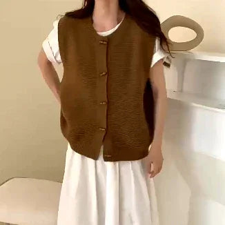 Woman wearing brown knit buttoned vest over white dress in minimal beige room