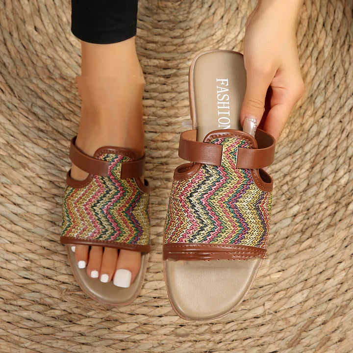 Pair of women's multicolor woven open-toe slide sandals with brown straps on woven mat