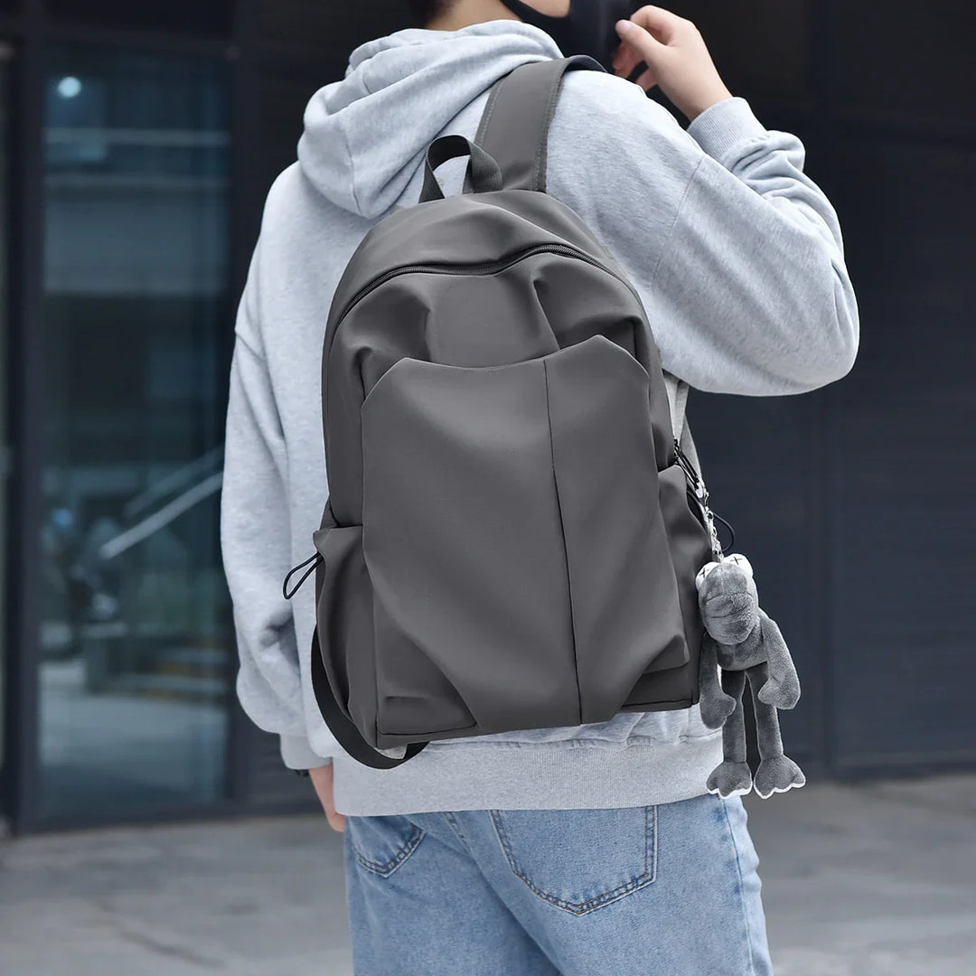 Person wearing grey hoodie and jeans carrying gray backpack with plush frog keychain