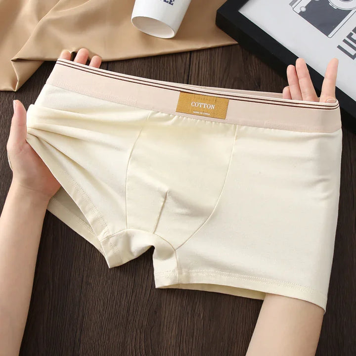 Hands stretching beige cotton men's boxer briefs with elastic waistband on wooden surface