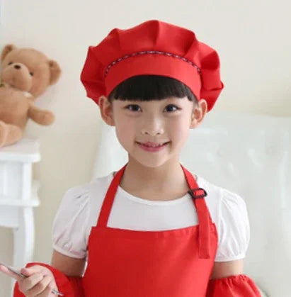 Smiling girl wearing red chef hat and apron in bright kitchen with teddy bear background