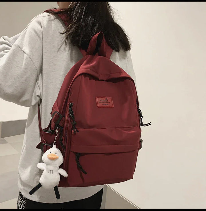 Person wearing light gray sweatshirt carrying dark red backpack with plush duck keychain