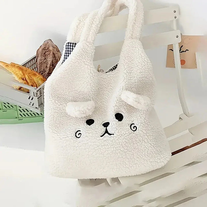 White fluffy teddy bear face tote bag hanging on white wooden chair with baked goods in background