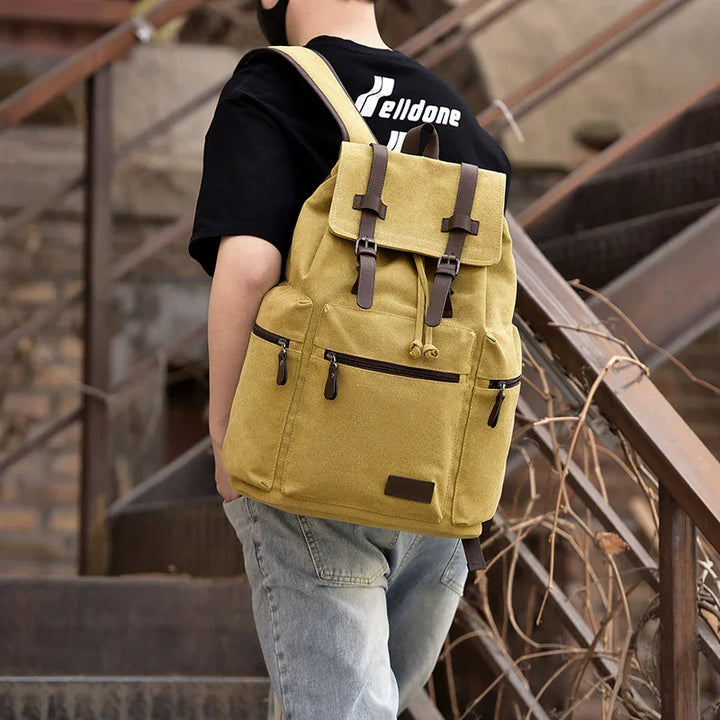 Person wearing a khaki canvas backpack with leather straps on stairs in urban outdoor setting
