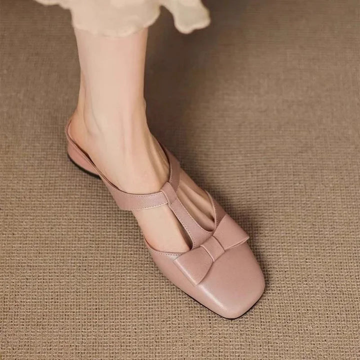 Woman wearing stylish pink leather T-strap flat shoes with bow detail on textured brown surface