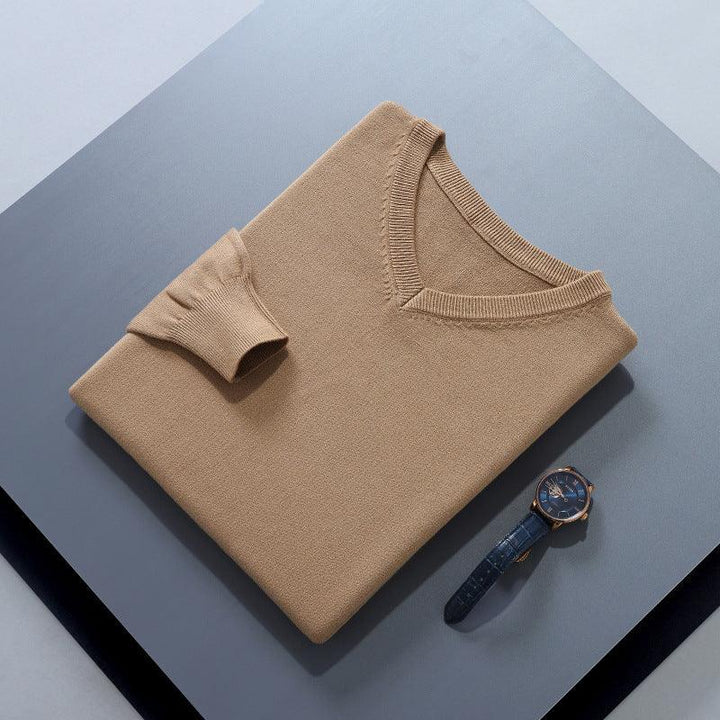 Folded beige v-neck sweater with long sleeves next to a blue leather strap wristwatch on a gray surface