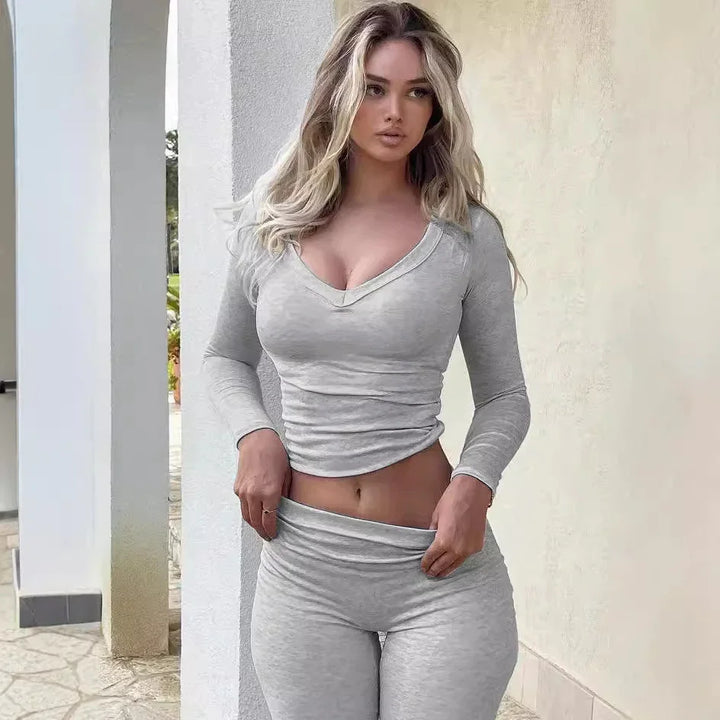 Woman in fitted light gray long-sleeve top and leggings outdoors near white pillars