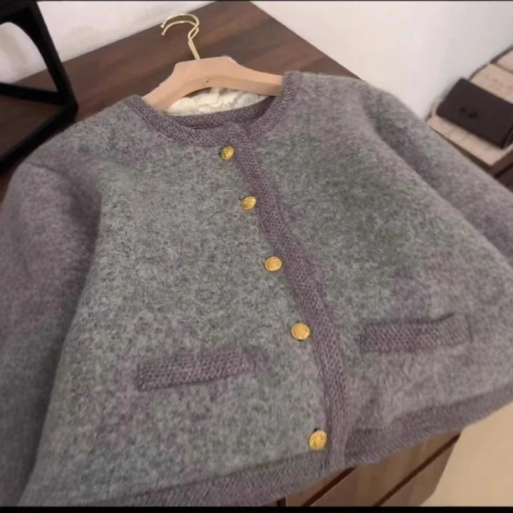 Gray wool cardigan with gold buttons hanging on wooden hanger on a table