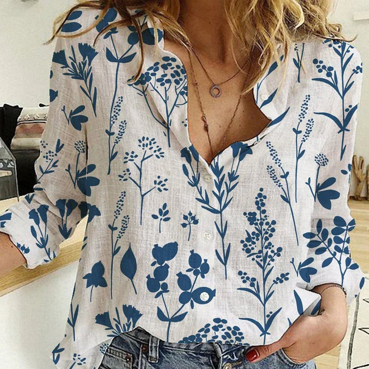 Woman wearing white blouse with blue botanical print and rolled-up sleeves indoors