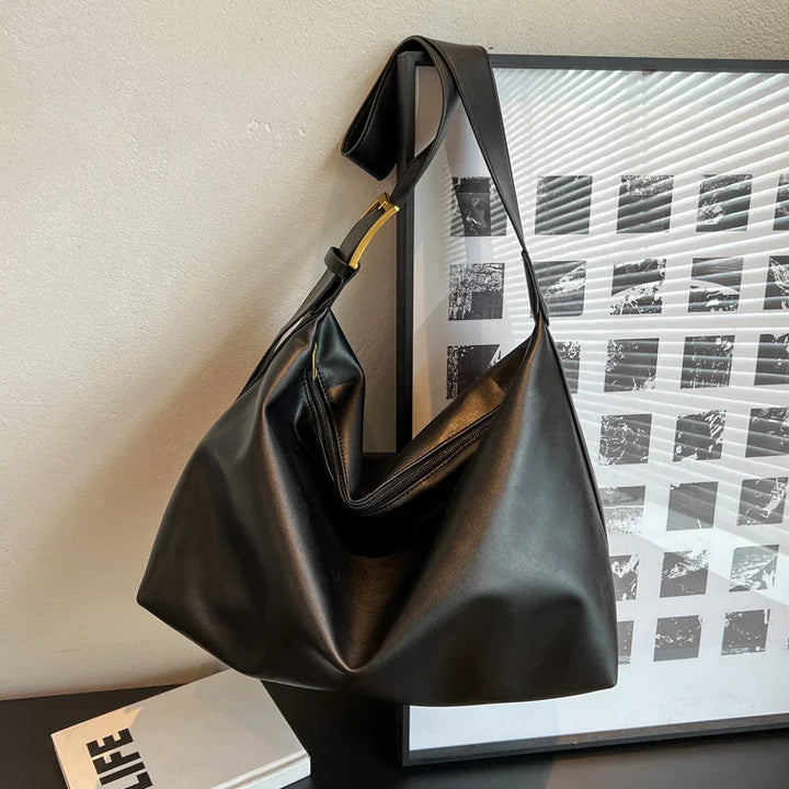 Black leather shoulder bag with gold buckle hanging on framed black and white abstract art