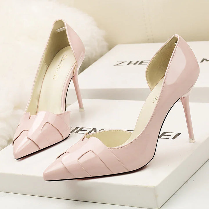 Pair of light pink patent leather high heel pumps with pointed toes and decorative front on white box