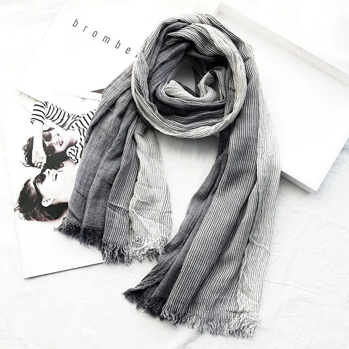 Gray and white striped lightweight scarf with fringed edges on white surface with black and white magazine