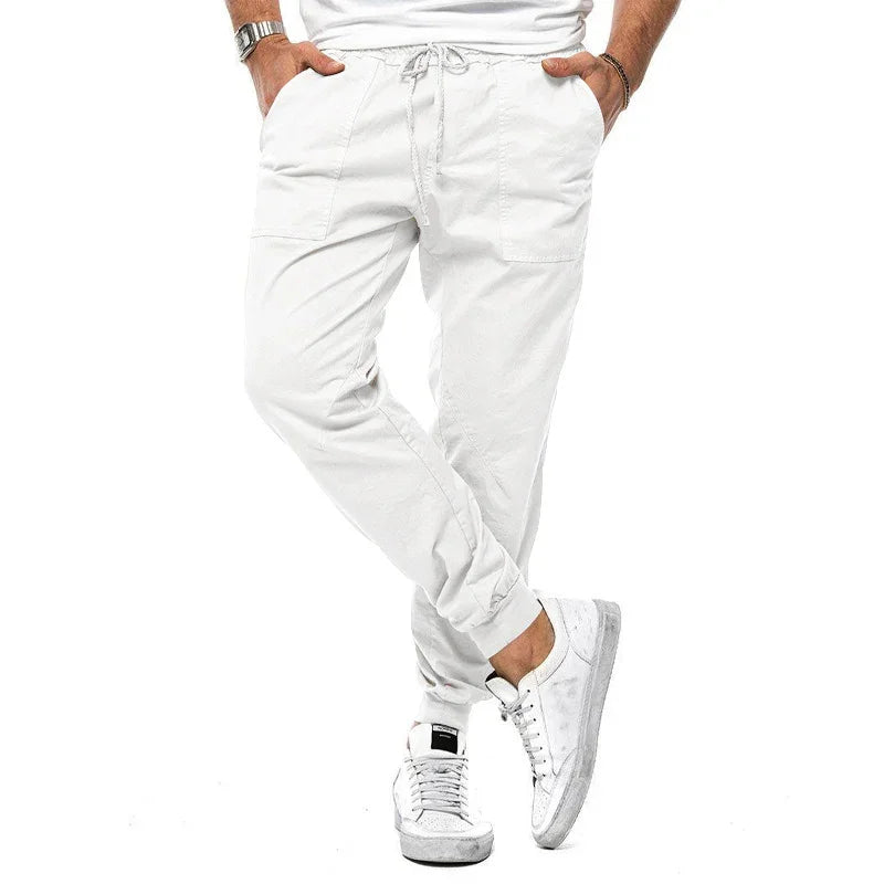 Men's white jogger pants with front pockets and drawstring waist, paired with white sneakers