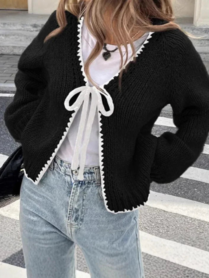 Woman wearing black knitted cardigan with white tie and trim over white top and light blue jeans