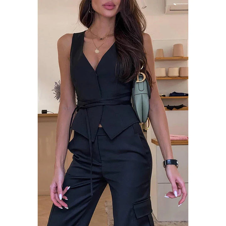 Woman wearing sleeveless black wrap top and black pants with green shoulder bag in boutique