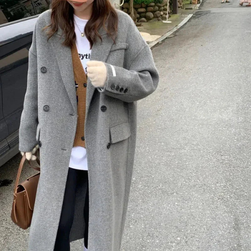Woman wearing long gray wool coat and brown cardigan on street holding brown leather handbag