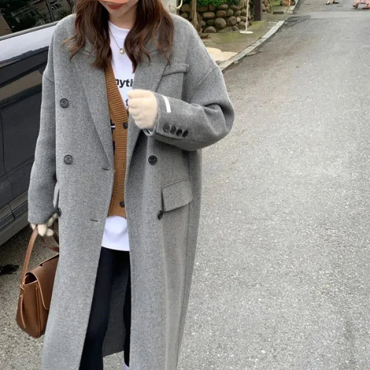 Woman wearing long gray wool coat and brown cardigan on street holding brown leather handbag