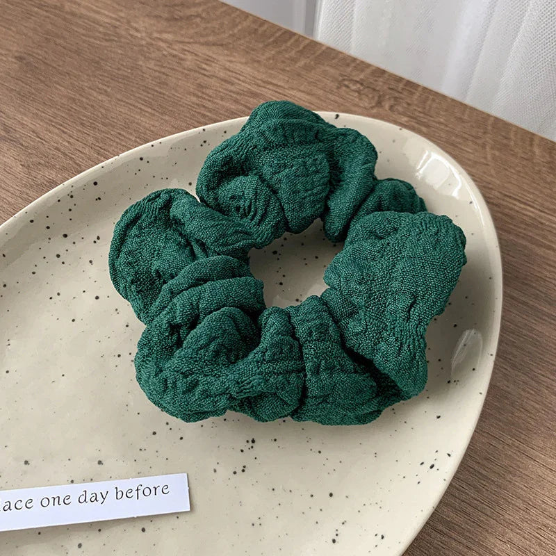 Green textured fabric scrunchie on a speckled ceramic plate on wooden surface