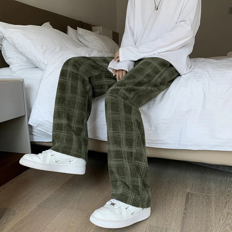 Person wearing white sneakers and olive green plaid pants sitting on a white bed in a modern bedroom