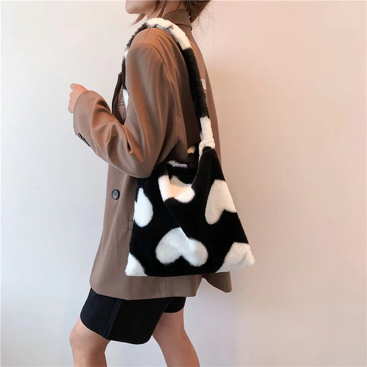 Woman wearing brown blazer and black shorts carrying black and white heart-patterned fuzzy shoulder bag