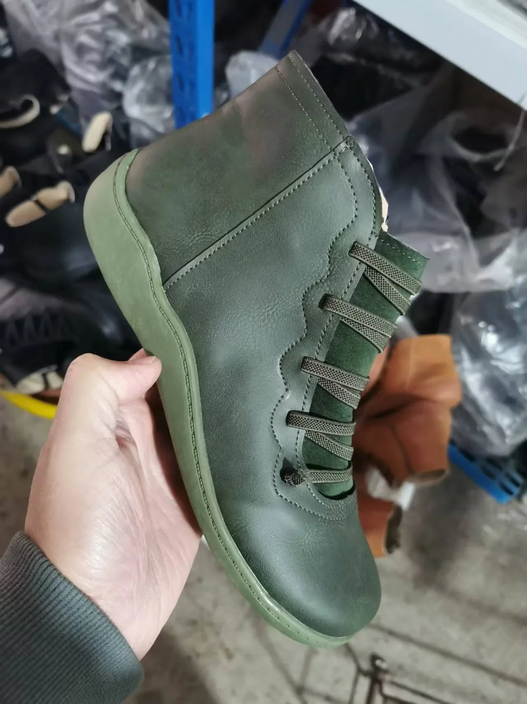 Hand holding green leather lace-up ankle boot with thick sole in shoe storage area