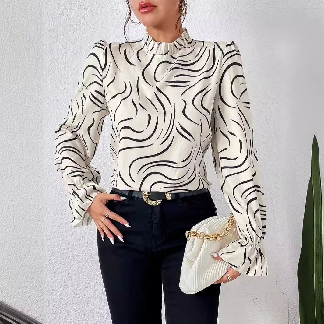 Woman wearing white blouse with black swirl pattern, paired with black pants and holding white clutch