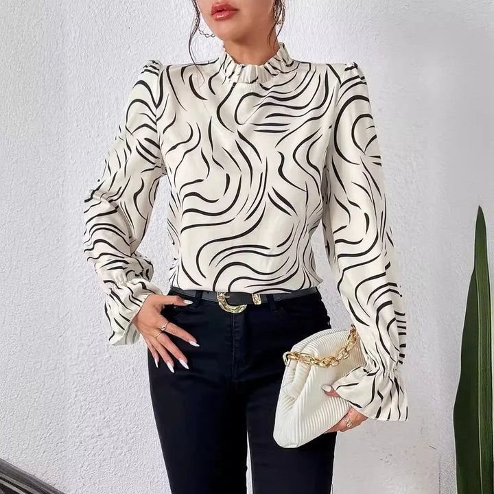 Woman wearing white blouse with black swirl pattern, paired with black pants and holding white clutch