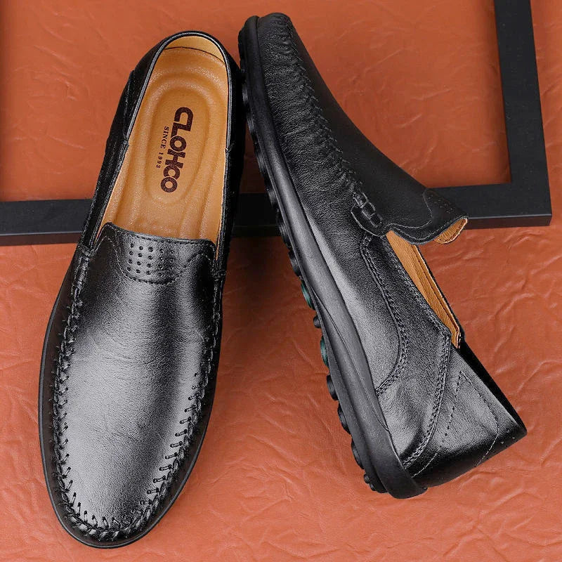 Black leather slip-on loafers with detailed stitching on brown textured surface