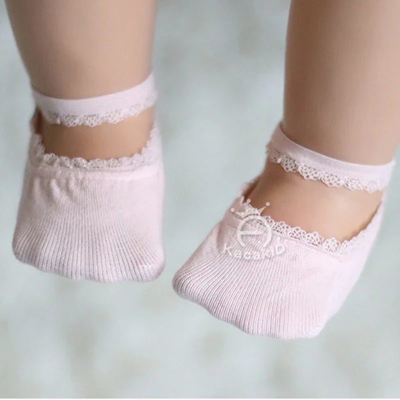 Baby feet wearing soft pink lace-trimmed ankle socks, close-up on light background