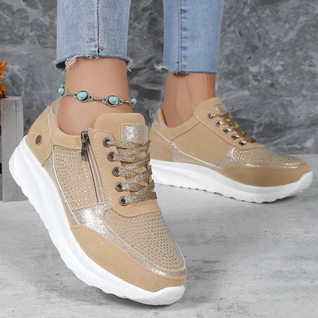 Beige and gold studded women's sneakers with white soles worn with light blue frayed jeans and turquoise ankle bracelet