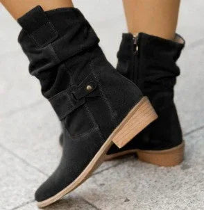 Black suede ankle boots with low wooden heels and side zipper on concrete pavement