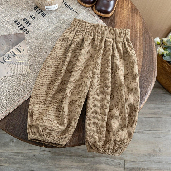 Beige floral patterned kids elastic waist corduroy pants on a wooden table with brown boots and Vogue magazine