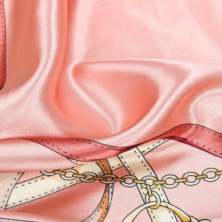 Close-up of pink silk scarf with chain and belt print, showcasing smooth, shiny fabric texture