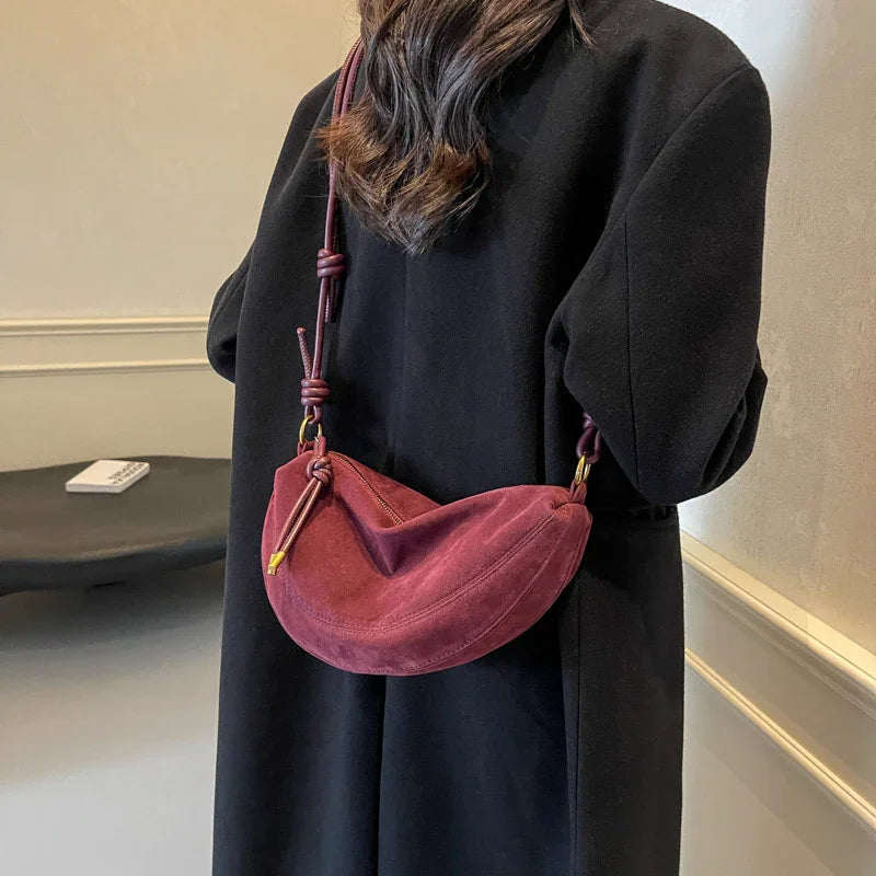 Woman in black coat carrying a crescent-shaped burgundy suede shoulder bag with knotted strap