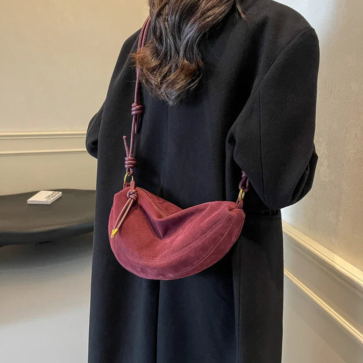 Woman in black coat carrying a crescent-shaped burgundy suede shoulder bag with knotted strap