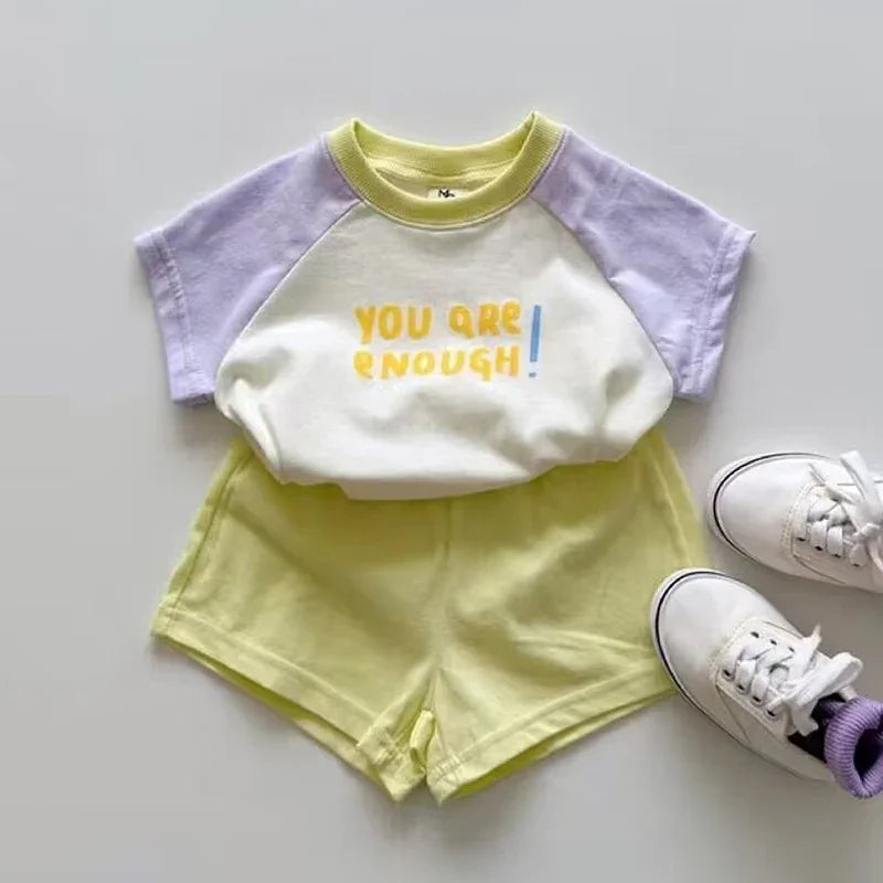 Kids outfit with a white and lavender short-sleeve top saying 'You are enough' paired with yellow shorts and white sneakers